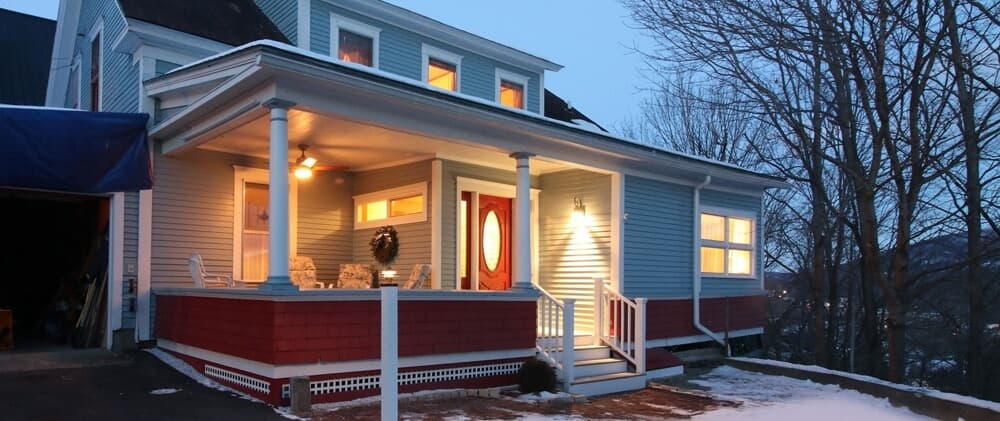 A cozy blue house with a red accent, featuring a welcoming porch and evening lighting.