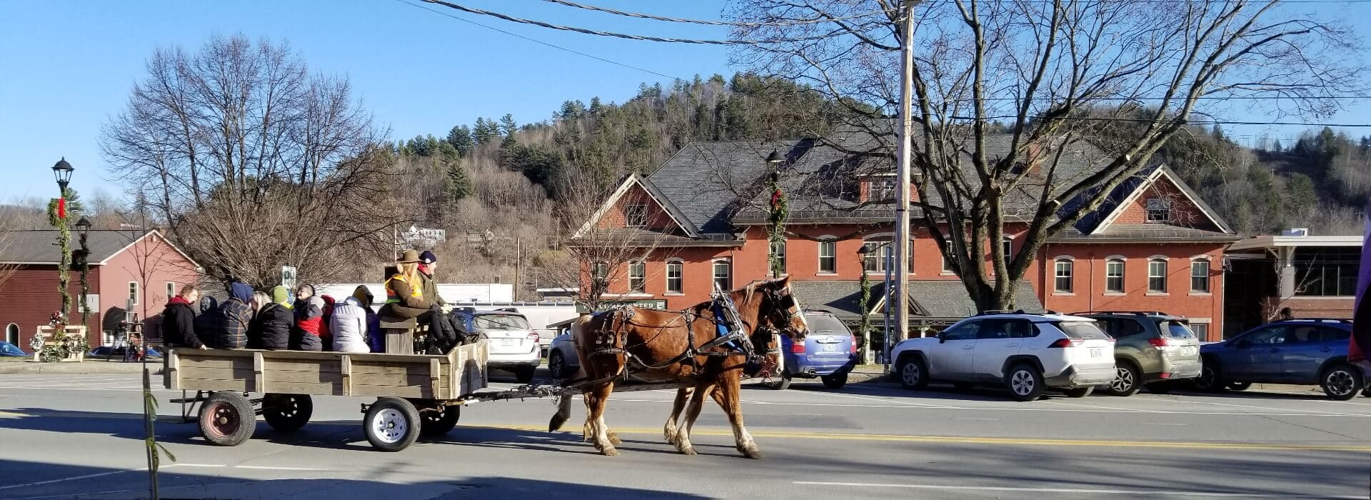 A horse-drawn wagon carries people through a small town on a clear day.