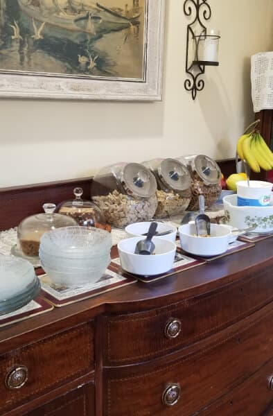 A wooden sideboard with bowls and glass containers filled with snacks, alongside a painting and a bunch of bananas.