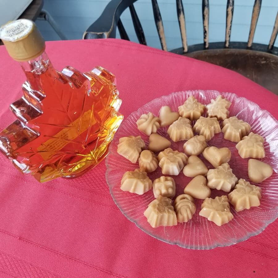 A maple syrup bottle next to a plate of assorted shaped candies on a red tablecloth.