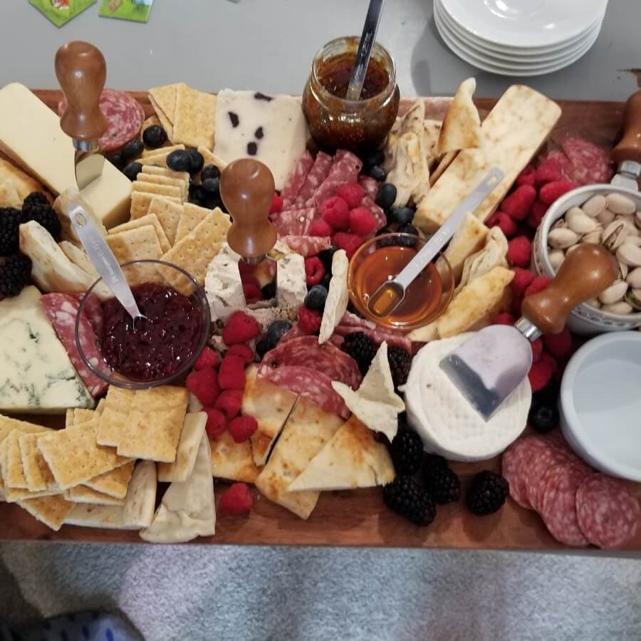A beautifully arranged cheese and charcuterie board with various cheeses, cured meats, fruits, crackers, and condiments.