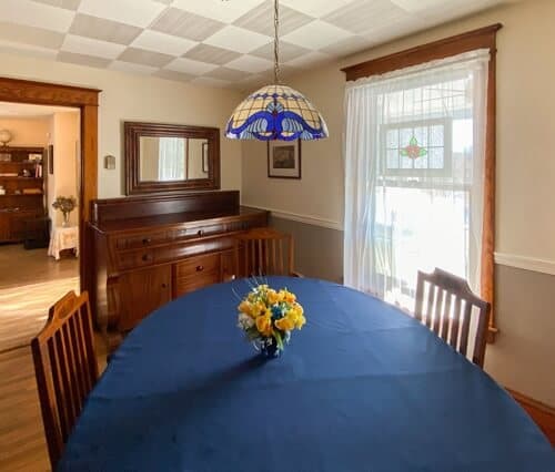 A cozy dining room with a blue tablecloth, vintage chandelier, and a vase of yellow flowers.
