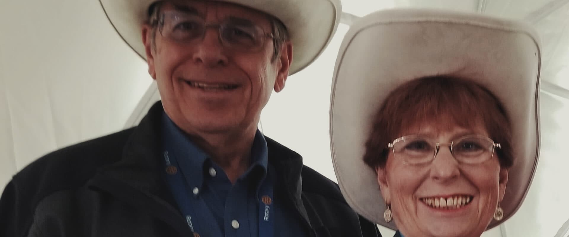 A smiling couple wearing cowboy hats poses for the camera.