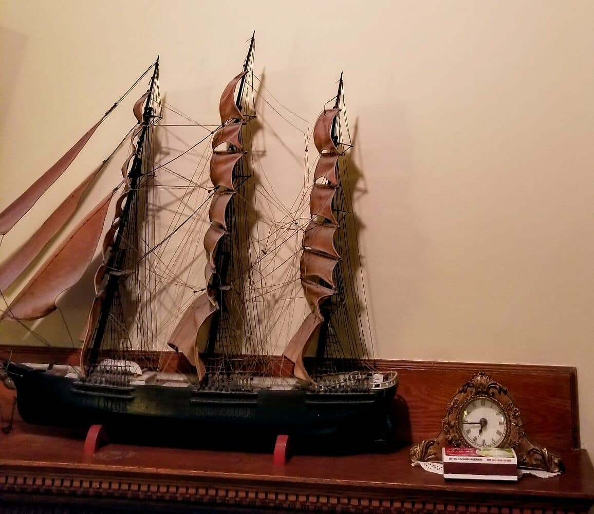 A detailed model of a tall ship displayed on a shelf next to an ornate clock and a stack of books.