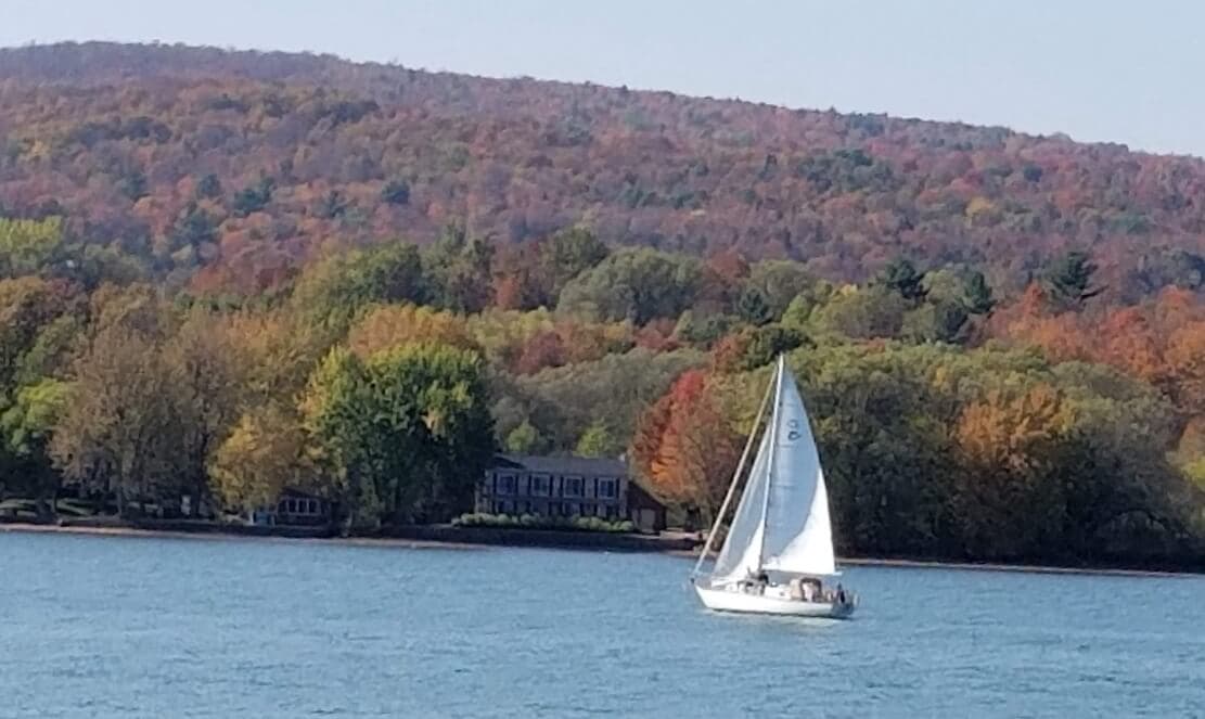 A sailboat glides on a lake surrounded by colorful autumn foliage.