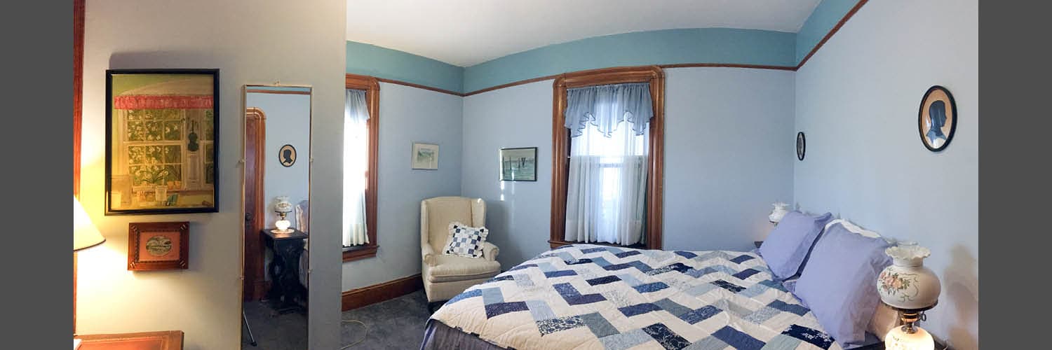 Cozy bedroom with blue walls, a quilted bed, and vintage decor, featuring a chair and a mirror.