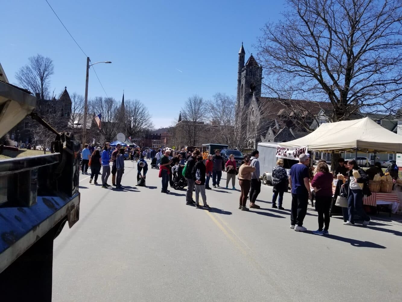 A crowded street festival with people gathered near food stalls and church buildings under a clear blue sky.