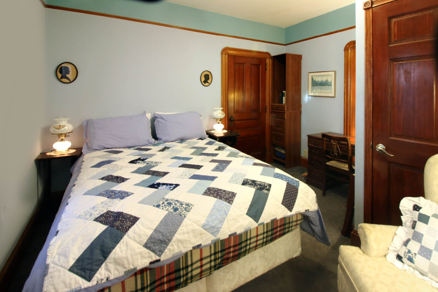 A cozy bedroom featuring a quilted bedspread, wooden furniture, and soft lighting.