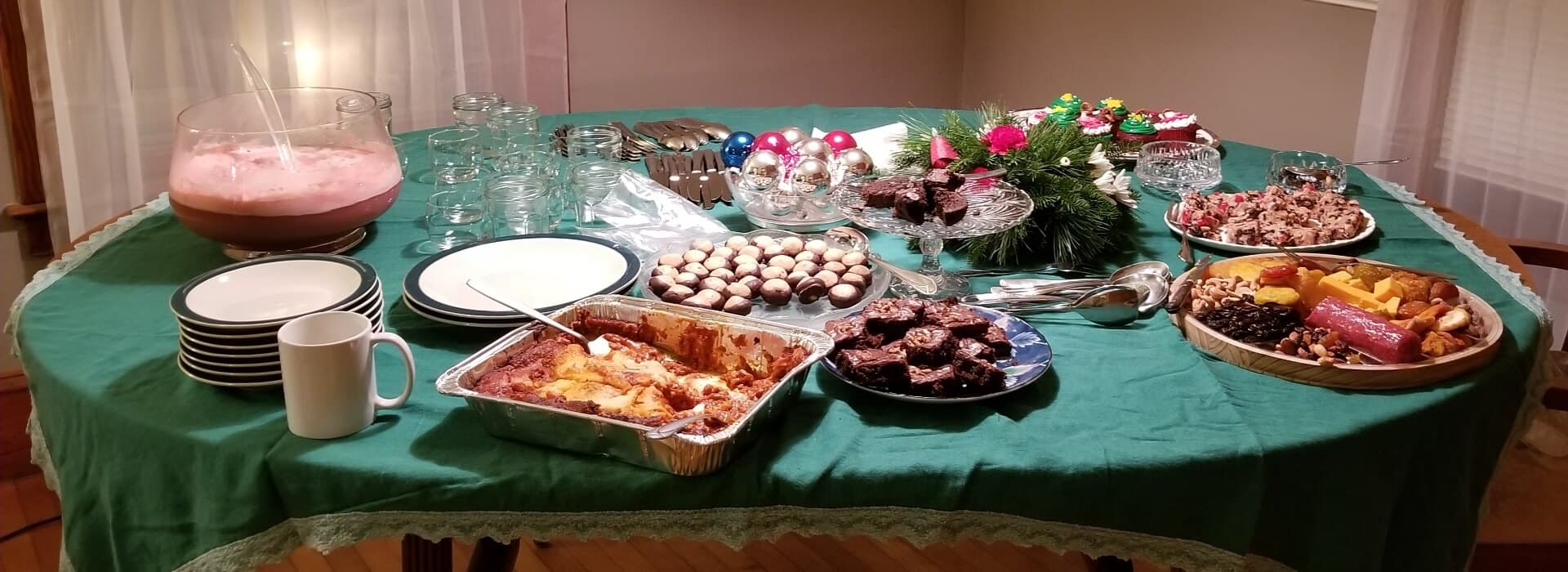 A table covered with a green cloth displays an assortment of festive food, drinks, and holiday decorations.