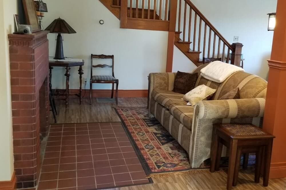 A cozy living room featuring a striped sofa, a small wooden table, a lamp, and a fireplace with a patterned rug.